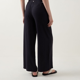Model wearing Tala Resort Drawstring Flared Trousers in Shadow Black, showing elasticated drawstring waist and wide-leg silhouette from behind.