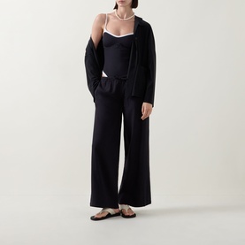 Model wearing Tala Resort Drawstring Flared Trousers in Shadow Black with matching black cami and cardigan, styled with pearl necklace and flat