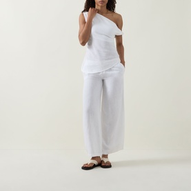 Model wearing Tala Soft Wide Leg Trousers in ivory, wide-leg linen blend with elasticated waist, styled with white one-shoulder top and brown sandals