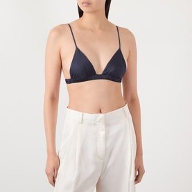 Model wearing The Frankie Shop navy viscose triangle bralette top with thin straps, styled with white wide-leg trousers.