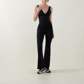 Model wearing Tala Shadow Black flared leggings with matching black V-neck top, styled with grey chunky trainers.