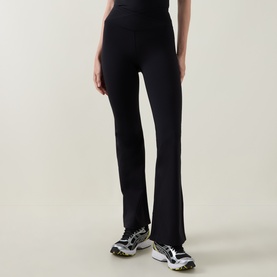 Model wearing Tala Shadow Black flared leggings in nylon-lycra blend, styled with white and yellow chunky trainers.