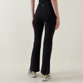 Model wearing Tala Shadow Black flared leggings, high-waisted with subtle logo detail, styled with yellow-accented trainers.