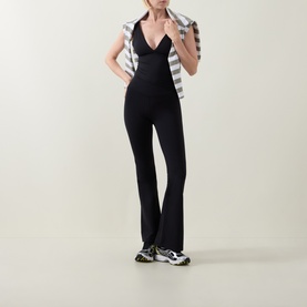 Model wearing Tala Shadow Black flared leggings with deep V-neck bodysuit, styled with striped jacket and chunky trainers.
