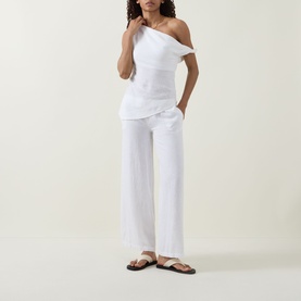 Model wearing Tala ivory one-shoulder linen-viscose top, styled with wide-leg white trousers and black flat sandals.