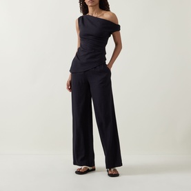 Model wearing Tala Shadow Black off-shoulder ruched linen-viscose top, styled with wide-leg trousers and flat sandals.