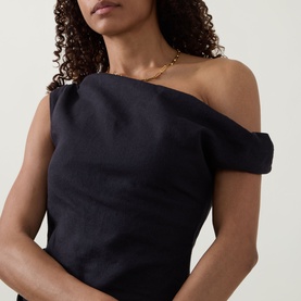 Model wearing Tala Shadow Black one-shoulder linen-viscose top with structured off-shoulder neckline, styled with a gold chain necklace.