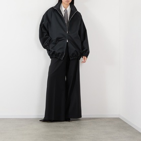 Model wearing The Frankie Shop white and black stripe shirt, styled with black oversized zip-up jacket and wide-leg trousers.