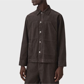 Model wearing All Saints dark brown corduroy shirt jacket with button front, chest pocket, and spread collar, styled with matching trousers.