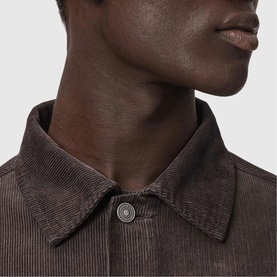 Model wearing All Saints dark brown corduroy shirt, close-up of point collar and gunmetal button detail.