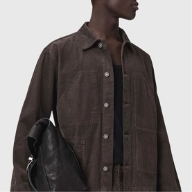 Model wearing All Saints dark brown corduroy overshirt jacket with silver buttons, styled with black tank and carrying black leather bag