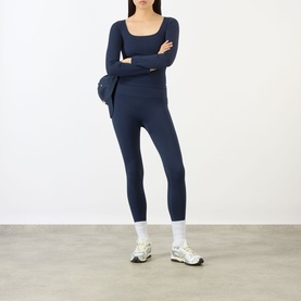 Model wearing Adanola navy blue leggings with matching long-sleeve top, styled with white trainers and socks, arms crossed.