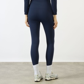 Model wearing Adanola navy blue leggings, shown from behind, styled with a matching navy long-sleeve top and white trainers.
