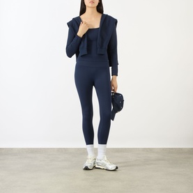 Model wearing Adanola navy blue leggings, styled with matching crop top, open jacket, white socks and chunky trainers, carrying a small bag.