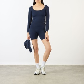 Model wearing Adanola navy blue cycling shorts with matching long-sleeve top, white socks and trainers, holding a cap.