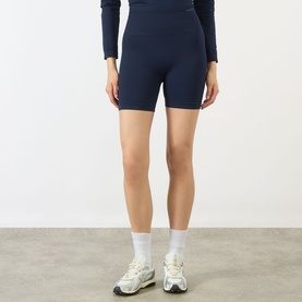 Model wearing Adanola navy blue seamless cycling shorts, styled with matching long-sleeve top and white trainers.
