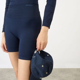 Model wearing Adanola navy blue cycling shorts with matching long-sleeve top. Model holds a navy cap.