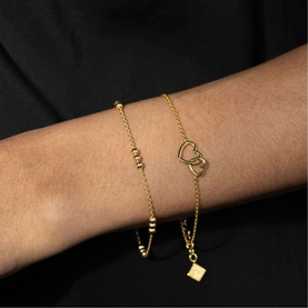 Model with Juvi gold-tone bracelets; delicate chain with beaded detail and open heart charm bracelet with square pendant drop