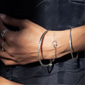 Model with Juvi silver bracelets stacked on wrist, including herringbone chain, hoop link, and cuff styles