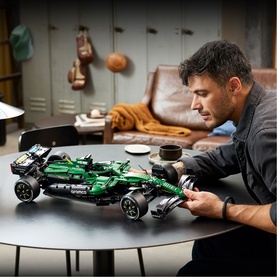 Adult assembling Lego Technic green Formula 1 racing car model on a table, with completed build visible in the foreground