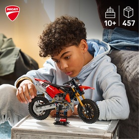 Boy building Lego Technic Ducati motocross bike model, red and white design, 457 pieces, ages 10 plus