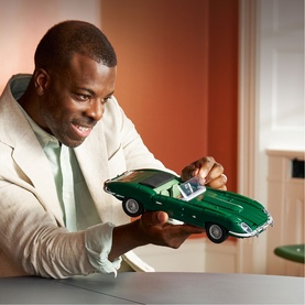 Model with Lego Icons Jaguar E-Type build, dark green scale model car held in both hands, wearing cream blazer