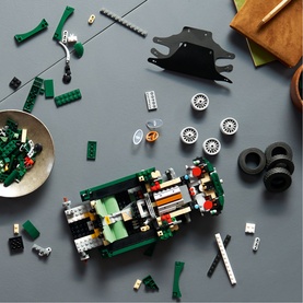 Lego Icons set with green car build in progress, surrounded by loose bricks, tyres, and components on grey surface
