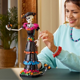 Lego Ideas Catrina skeleton figure toy in multi-coloured floral dress, shown with smiling model assembling the set