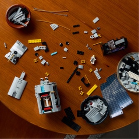 Lego Icons set with multi-coloured bricks and partially built structures spread across a wooden table, with sorted pieces in bowls