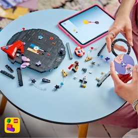 Lego Editions Music toy set displayed on table with colourful brick pieces, circular base, and tablet showing building guide app