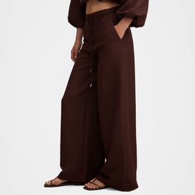 Model wearing Forever New chocolate wide-leg tailored trousers with front pleats, styled with brown strappy flat sandals