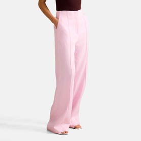 Model wearing Forever New wide-leg trousers in Candy Hearts pink, high-waisted with a tailored silhouette, styled with a dark top and beige heels.