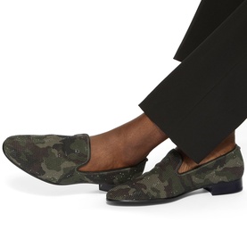 Model wearing Kurt Geiger London green camouflage slip-on loafers with mesh detail and navy sole, styled with black tailored trousers.