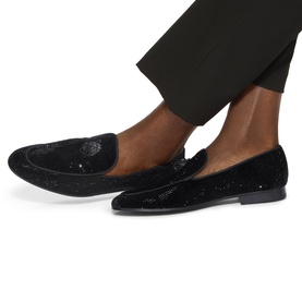 Model wearing Kurt Geiger London black sequin embellished velvet loafers, styled with black tailored trousers.