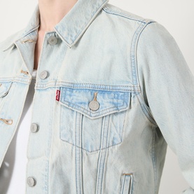 Model wearing Levi's The Original Trucker Jacket in De Oro Trucker light wash denim, showing chest flap pockets and tobacco stitching detail.