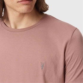 Model wearing a dusty pink crew neck T-shirt with small AllSaints Ramskull logo embroidered on chest.