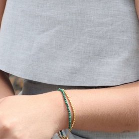 Model with Juvi Amalfi Double Bracelet in green malachite and gold-toned beads, worn on wrist, styled with grey linen top