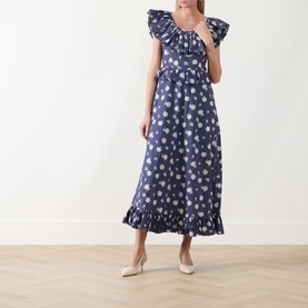 Model wearing Queens of Archive Devon Prairie Floral Dress in Prairie Rose Blue with frill neck and hem, styled with cream heeled mules