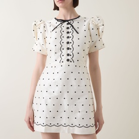Model wearing Queens of Archive Suki Mini Dress in White Polka with black bow, covered buttons, scallop trim and puff sleeves