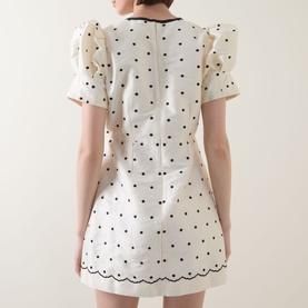 Model wearing Queens of Archive Suki Mini Dress in White Polka, showing rear view with structured sleeves, scallop hem trim, and polka dot print.
