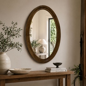 Mindy Browne Osian Wall Mirror in brown wood frame, oval shape, hung above a rustic console table in a neutral styled room