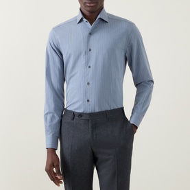 Model wearing Corneliani Herringbone Tonal Striped Shirt in mid blue with spread collar and front button fastening, styled with grey trousers.
