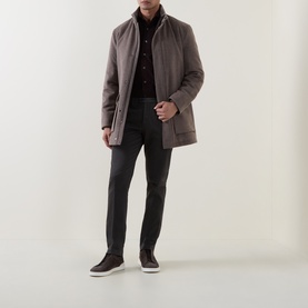 Model wearing a taupe padded zip-up jacket with stand collar, styled with dark trousers and brown suede shoes
