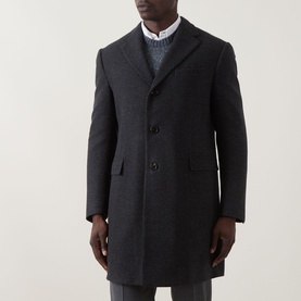 Model wearing dark charcoal single-breasted wool overcoat with notch lapels, three-button front, and flap pockets, styled with white shirt