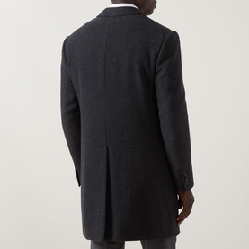 Model wearing a dark charcoal wool overcoat, rear view showing tailored back vent and structured shoulders, styled with white shirt.