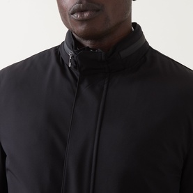 Model wearing Corneliani Technical Padded Coat in black, close-up of high zip-up neckline with gunmetal hardware detail.