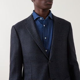 Model wearing Corneliani navy wool check blazer jacket, styled with a blue denim shirt, notch lapels visible.