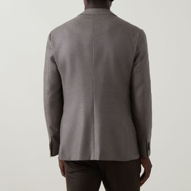 Model wearing Corneliani stone virgin wool and cashmere jacket, rear view showing tailored seam detail and button cuffs, styled with dark trousers.