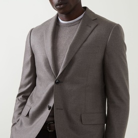 Model wearing Corneliani stone wool-cashmere blazer with notch lapels and two-button fastening, styled with a grey crew-neck knit and brown belt.