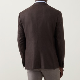 Model wearing Corneliani brown virgin wool jacket, rear view, showing clean back seam, side vents, and grey trousers